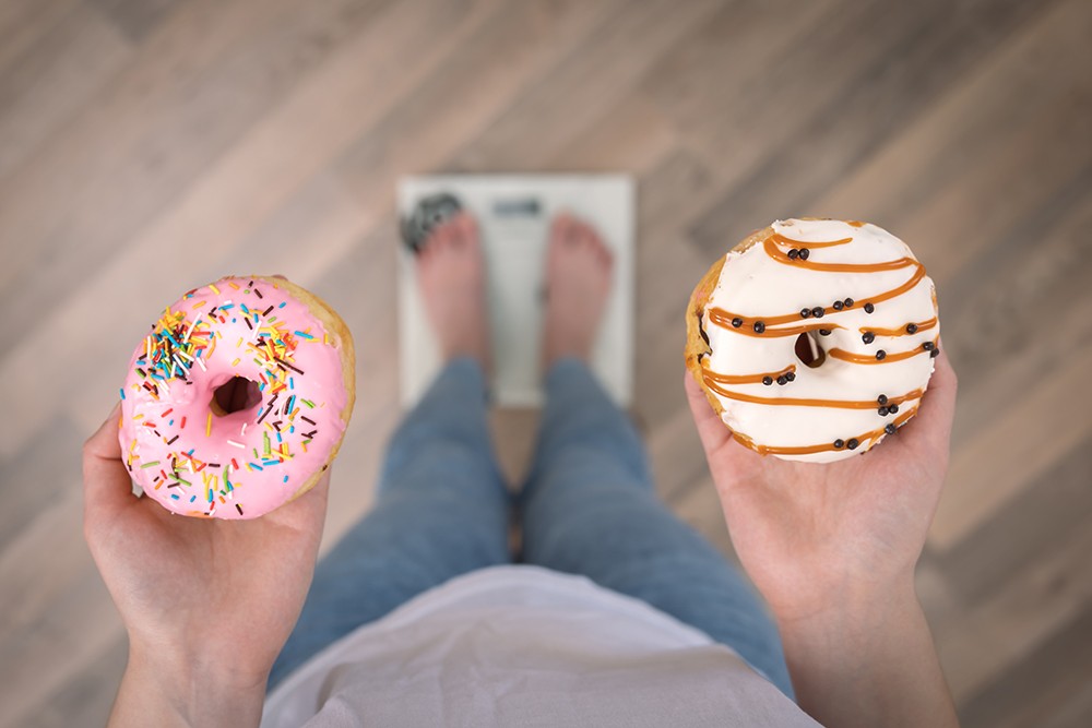 woman-stands-scales-holds-donuts-her-hands-top-view-copy-space.jpg